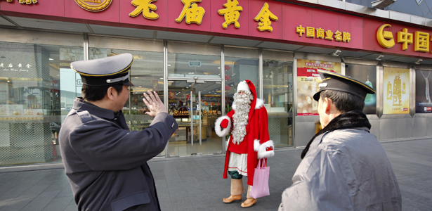 A man dressed as Santa Claus walks past two security guards in downtown Shanghai December 23, 2010. Officially recognized by the Finland government after a four-year training, the man is one of 50 officially registered Santa Clauses who is paying a visit to Shanghai, warming up the Christmas holidays. REUTERS/Aly Song (CHINA - Tags: SOCIETY IMAGES OF THE DAY)